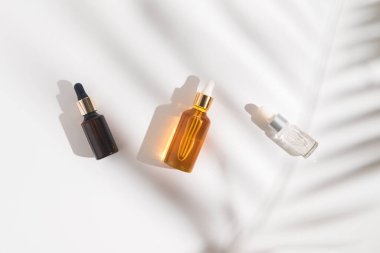 Beyaz arka planda beyaz, turuncu ve siyah serum şişeleri. Palmiye dalının gölgesi. Kozmetik modeli. Metin ve resimler eklenecek yer. Üst Manzara. Düz yatıyordu.