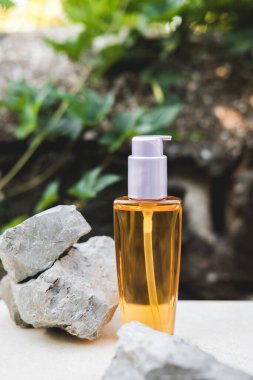 Doğal taşların yanında turuncu bir yağ şişesi. Gri bir duvara karşı doğal ışık. Moda tarzı. Kozmetik modeli. Kopyalama alanı.