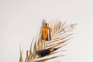 Beyaz arka planda beyaz, turuncu ve siyah serum şişeleri. Palmiyelerin altın dalları. Kozmetik modeli. Metin ve resimler eklenecek yer. Üst Manzara. Düz yatıyordu.