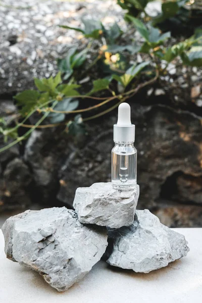 Botellas de suero transparente junto a piedras naturales contra una pared gris con luz natural. Estilo de moda. Una maqueta cosmética. Espacio de copia. —  Fotos de Stock