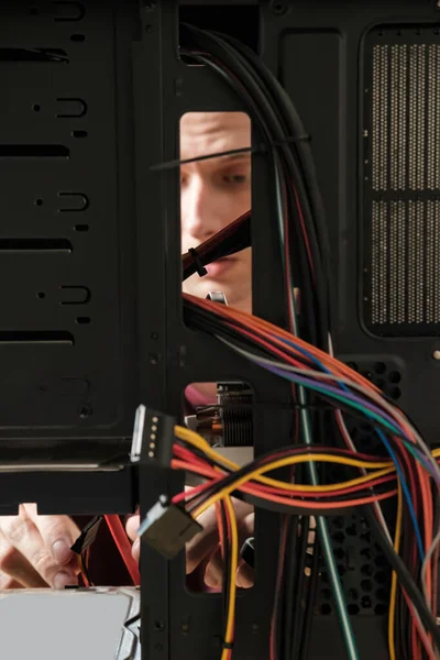 Young man repairs a computer system unit, changes parts, video card and hard drive, sets new components. Computer Repair Wizard.