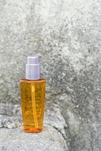 Una botella de aceite de naranja junto a piedras naturales contra una pared gris con luz natural. Estilo de moda. Una maqueta cosmética. Espacio de copia. —  Fotos de Stock