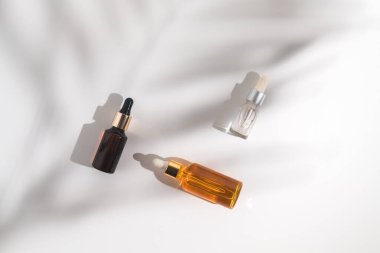 Beyaz arka planda beyaz, turuncu ve siyah serum şişeleri. Palmiye dalının gölgesi. Kozmetik modeli. Metin ve resimler eklenecek yer. Üst Manzara. Düz yatıyordu.