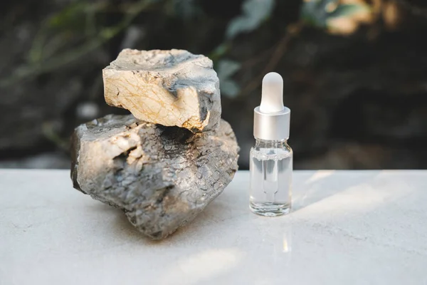 Botellas de suero transparente junto a piedras naturales contra una pared gris con luz natural. Estilo de moda. Una maqueta cosmética. Espacio de copia. —  Fotos de Stock