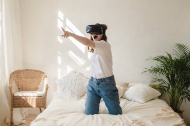 Kot pantolonlu ve kafasında sanal gerçeklik gözlüğü olan beyaz tişörtlü genç bir kadın kollarını oynatıyor, dans ediyor, korkuyor. Modern teknoloji kavramı, VR, sanal oyunlar, eğlence..