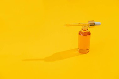 Parlak sarı arka planda parlak ışık gölgesiyle turuncu renkli serum şişeleri. Moda tarzı. Kozmetik modeli. Kopyalama alanı