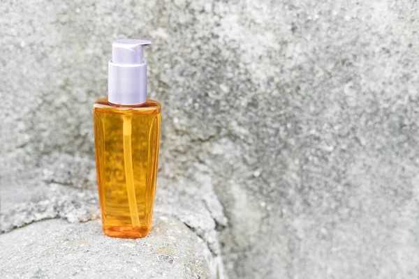 Una botella de aceite de naranja junto a piedras naturales contra una pared gris con luz natural. Estilo de moda. Una maqueta cosmética. Espacio de copia. —  Fotos de Stock