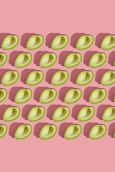 Трендовый узор в стиле полубезсеменного зеленого авокадо на розовом фоне с жестким светом. Творческая текстура продуктов питания. — стоковое фото