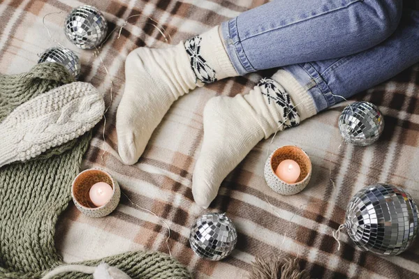 Junge Frau sitzt auf dem Bett in kuscheligem Strickpullover, Socken und hält Spielzeug-Discokugel in den Händen. Hygge, Kerzen, Silvester, Weihnachten, Feiertagsvorbereitungen. — Stockfoto