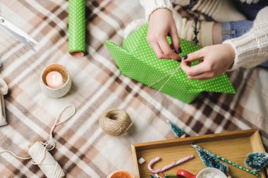 Genç kadın rahat örülmüş yün beyaz kazak, çorap ve Noel hediyesini puantiyeli ambalaj kağıdına sarar. Tahta tepside bir kupa marshmallowlu kakao, oyuncak ağaç, mum, pipet..
