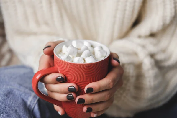 Young woman sits on plaid in cozy knitted woolen white sweater and holds cup of cocoa with marshmallows in her hands. Hygge New Year, cozy Christmas, preparation for holidays. — Stock Photo, Image