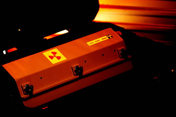 Box shaped metal container with radiation warning in a military grade transport box under red light