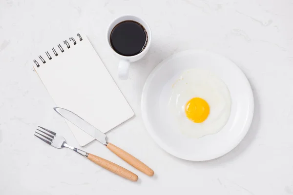 白色的笔记本 煎鸡蛋和咖啡杯白色的背景白碟的顶部视图 — 图库照片
