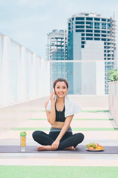 Image of happy young asian sports woman sitting outdoors talking on mobile phone.