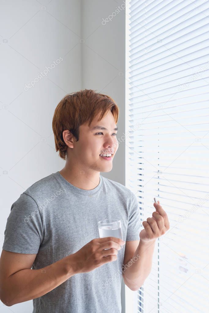 Happy asian man holding pill and glass of water