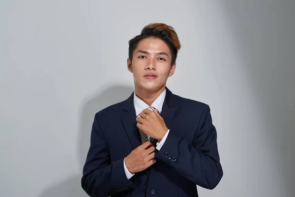 Confident businessman straightening his tie over gray background and looking at camera