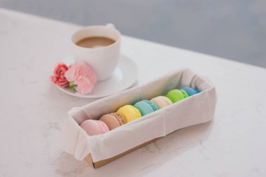 Fransızca macaroons hediye kutusu ve kahve Kupası beyaz masaya çiçek ile renk