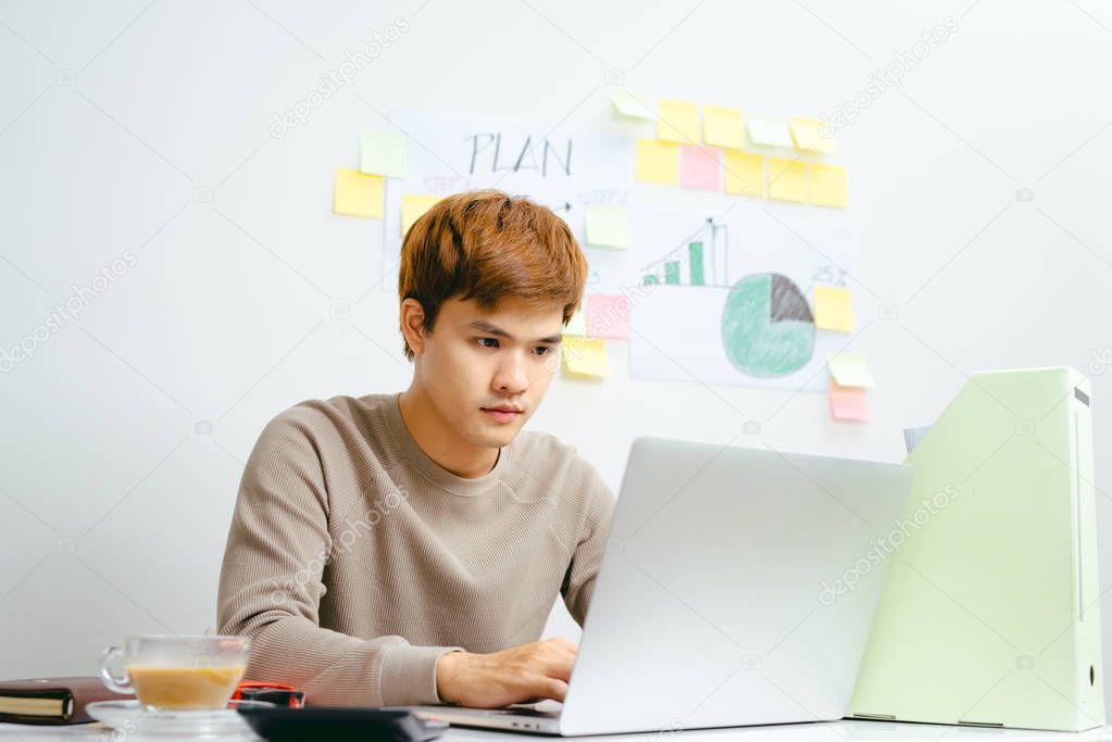 Unhappy Asian Businessman working on laptop sitting at table