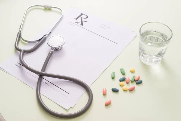 blank notepad, stethoscope, color pills and glass of water on light green background. medicine concept