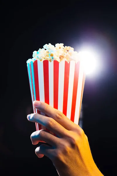 hand holding box with popcorn over cinema light background, movie concept