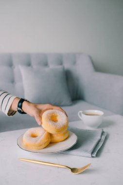 Yemek ve ekmek, şeker Toppings ile lezzetli taze ve tatlı çörek üzerinde beyaz çanak tutan el.