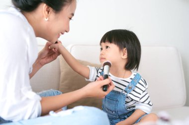 Sevimli küçük kız ve güzel annesi evde kanepede otururken makyaj yapıyorsun