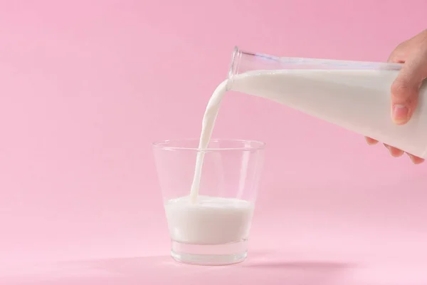 Pembe Bir Arka Plan Üzerinde Cam Içine Süt Dökme — Stok fotoğraf
