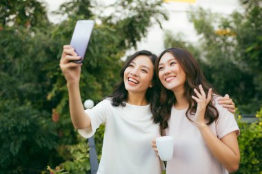 İki güzel mutluluk uzun saç kadınların yaşam biçimi kullanarak cep telefonu için Selfie bahçe vardır. Asyalı kadın modelleri portre kavramı.