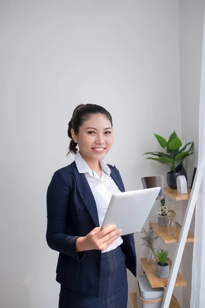 Strong, confident, Asian business woman standing in an office building hallway, holding tablet computer