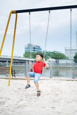 Mutlu Asyalı çocuk oyun park alanında, sallanan