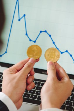 Fiziksel bitcoin ve ethereum cryptocurrency paralar grafiğin arka plan üzerinde onun elinde tutan adam