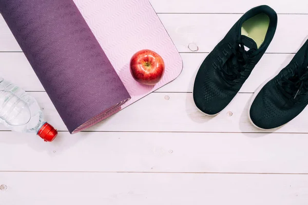 Ladies Sports Accessories such as trainers shoes, dumbbells, yoga mat with water and apple. Fitness, sport and healthy lifestyle concept. Top view, copy space