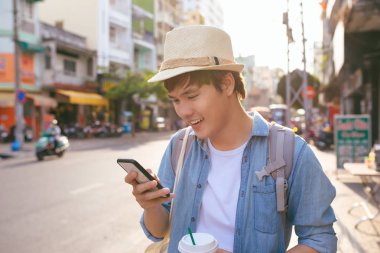 Kahve içme ve akıllı telefon kullanarak gülümseyen yakışıklı genç adam