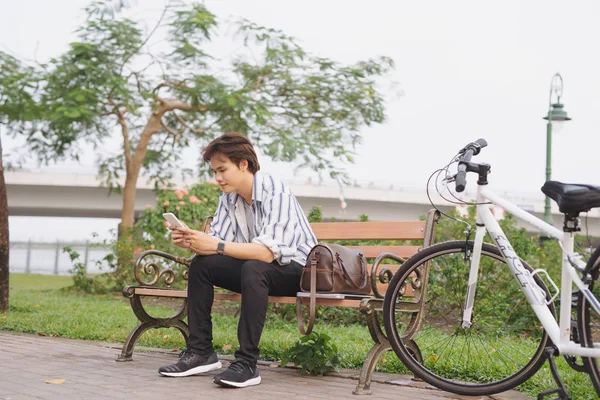 Jovem Usando Telefone Enquanto Sentado Banco Com Bicicleta Parque — Fotografia de Stock