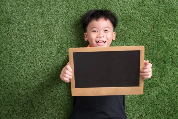 Bonito Ásia Criança Mentira Segurando Blackboard Verde Grama — Fotografia de Stock