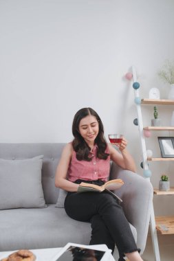 Genç kadın kanepede kitap okuma çay içme