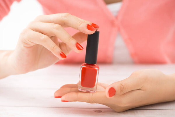 Female hands with red manicure and an open bottle of varnish on the table