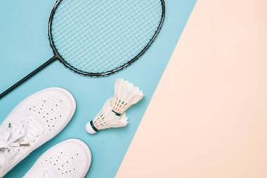 Pastel renk arka plan üzerinde spor ayakkabılarla raketle ve badminton raket