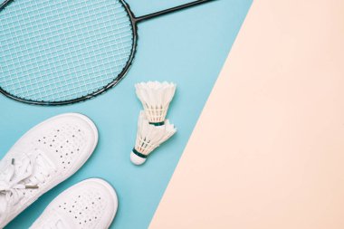Pastel renk arka plan üzerinde spor ayakkabılarla raketle ve badminton raket