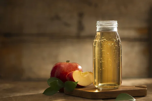 Apple juice in a bottle and glass with sliced red apple in wooden background