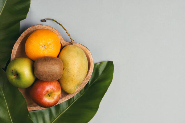 Orange, mango, apple and kiwi in a wooden heart-shaped plate