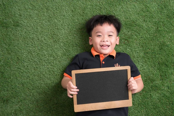 Söt Asiatiska Barn Ligga Och Hålla Blackboard Grönt Gräs — Stockfoto