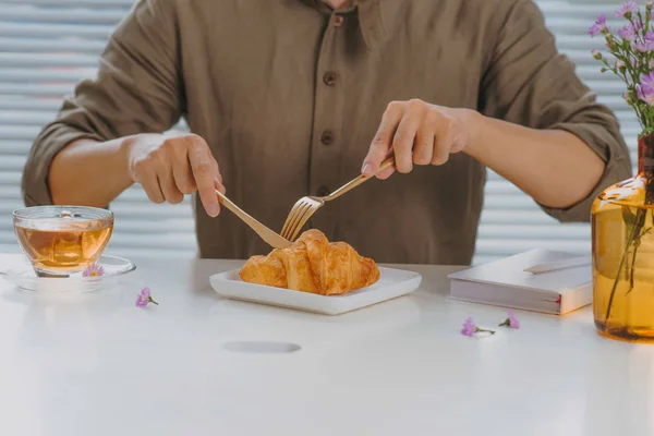 man eating fresh croissant siting at table at bakery shop