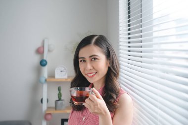 Genç kadın içme kahve veya çay iş veya evde eğitim sırasında gülümseyen