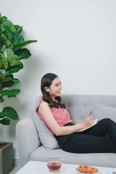 Woman flying at the couch, writing in the notebook in nice light home interior. Working at home. Freelancer. writing down ideas. indoors.