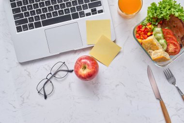 Cam dizüstü, portakal suyu ve taze salata işyerinde öğle yemeği kutusundaki üstten görünüm