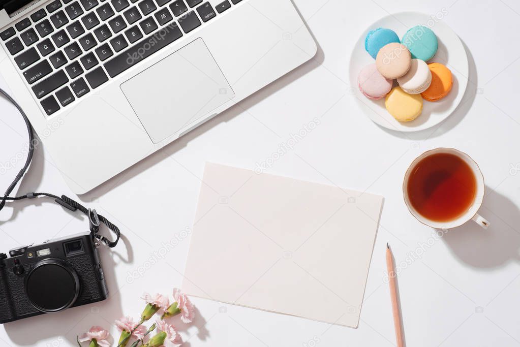 colorful macaroons, coffee cup, laptop and open blank notebook with pencil on white table