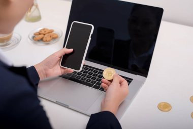 Bitcoin ofis masası üzerinde tutarak ve Smartphone'da yazarak genç kafkas kadın