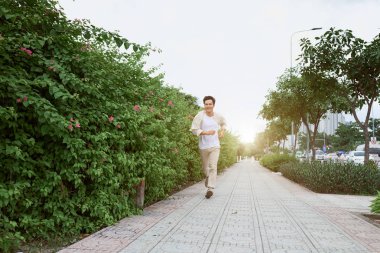 Yeşil yaz Park'ta koşan gülümseyen genç adam 