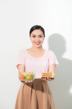 Varoluş küçük kek, tutan çok güzel kadın portresi taze sebze. Genç ev hanımı seçerek tatlılar ya da sağlıklı beslenme - kek ve salata. Beyaz arka plan üzerinde izole.